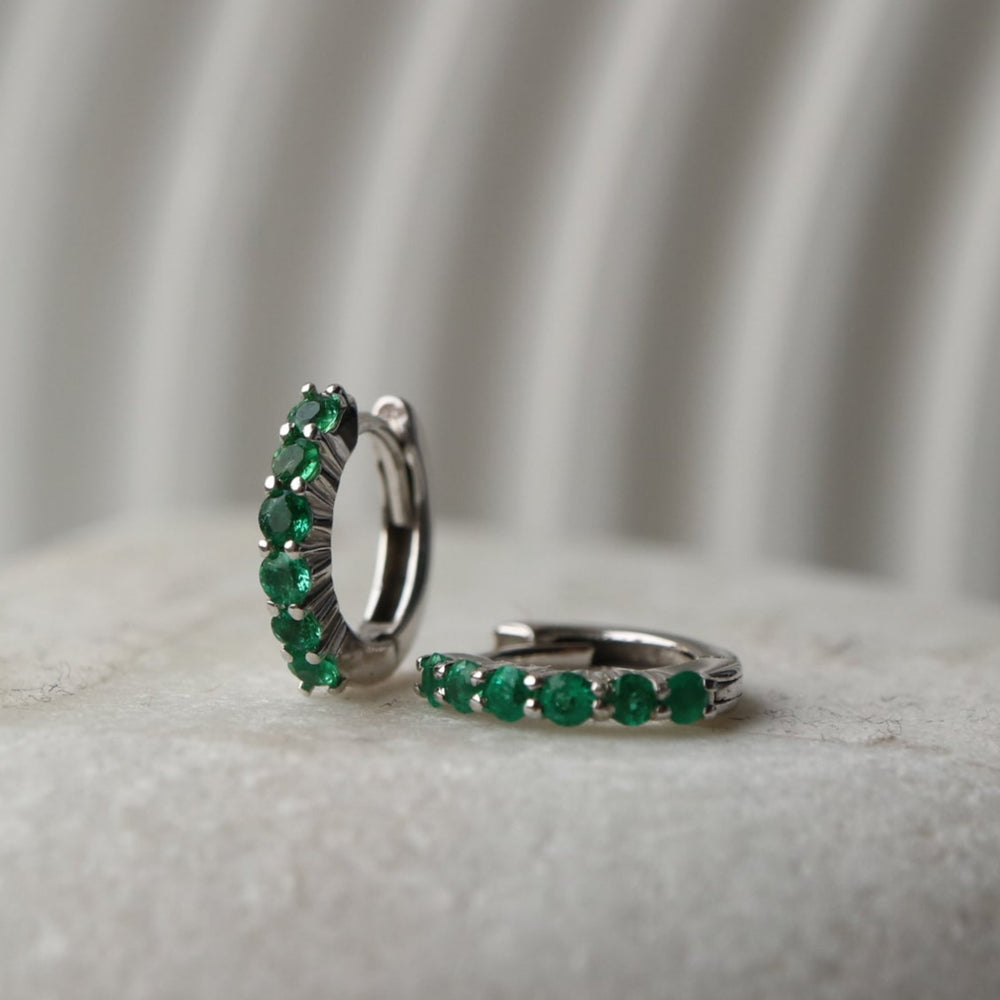 Zambian emerald huggie hoop earrings featuring six 2mm eye-clean emeralds set in rhodium-plated sterling silver, with a 12mm outer diameter