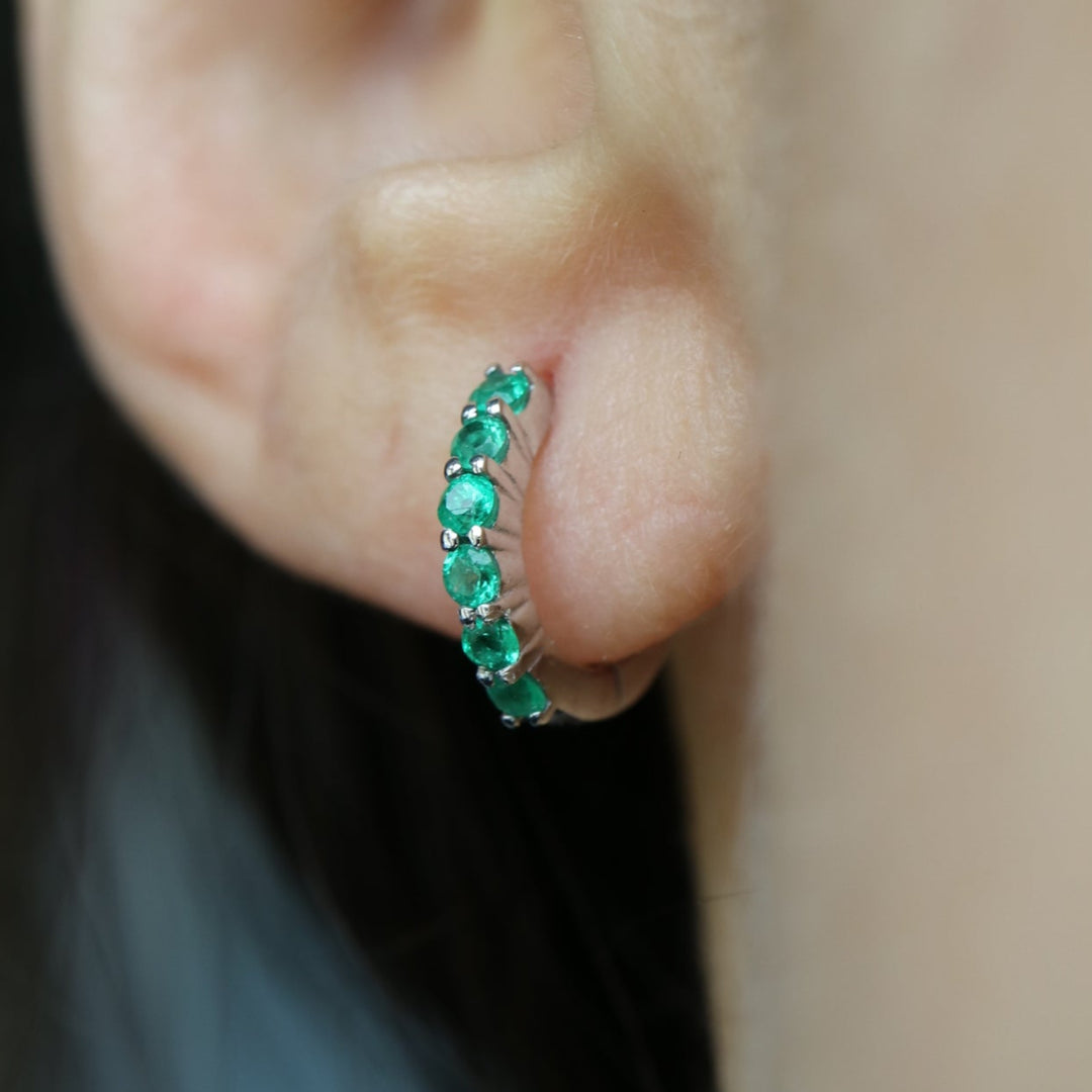 Zambian emerald huggie hoop earrings featuring six 2mm eye-clean emeralds set in rhodium-plated sterling silver, with a 12mm outer diameter